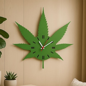 Op de afbeelding: Een groene wandklok in de vorm van een cannabisblad met zwarte uurmarkeringen en witte en rode wijzers. De klok is bevestigd aan een lichtbruine houten muur. Het ontwerp van de klok is een uniek decoratief stuk.