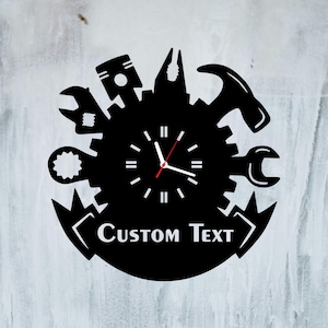 May include: Black wall clock featuring tools like a wrench, hammer, and pliers arranged around a clock face. The clock has white hands and a red second hand. The words "CUSTOM TEXT" are displayed at the bottom.
