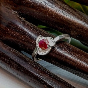 Könnte beinhalten: Ein silberner Ring mit einem roten Edelstein, der in einem herzförmigen Design gefasst ist.