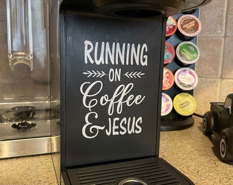 Może przedstawiać: Czarny ekspres do kawy z białym napisem "Running on Coffee & Jesus".