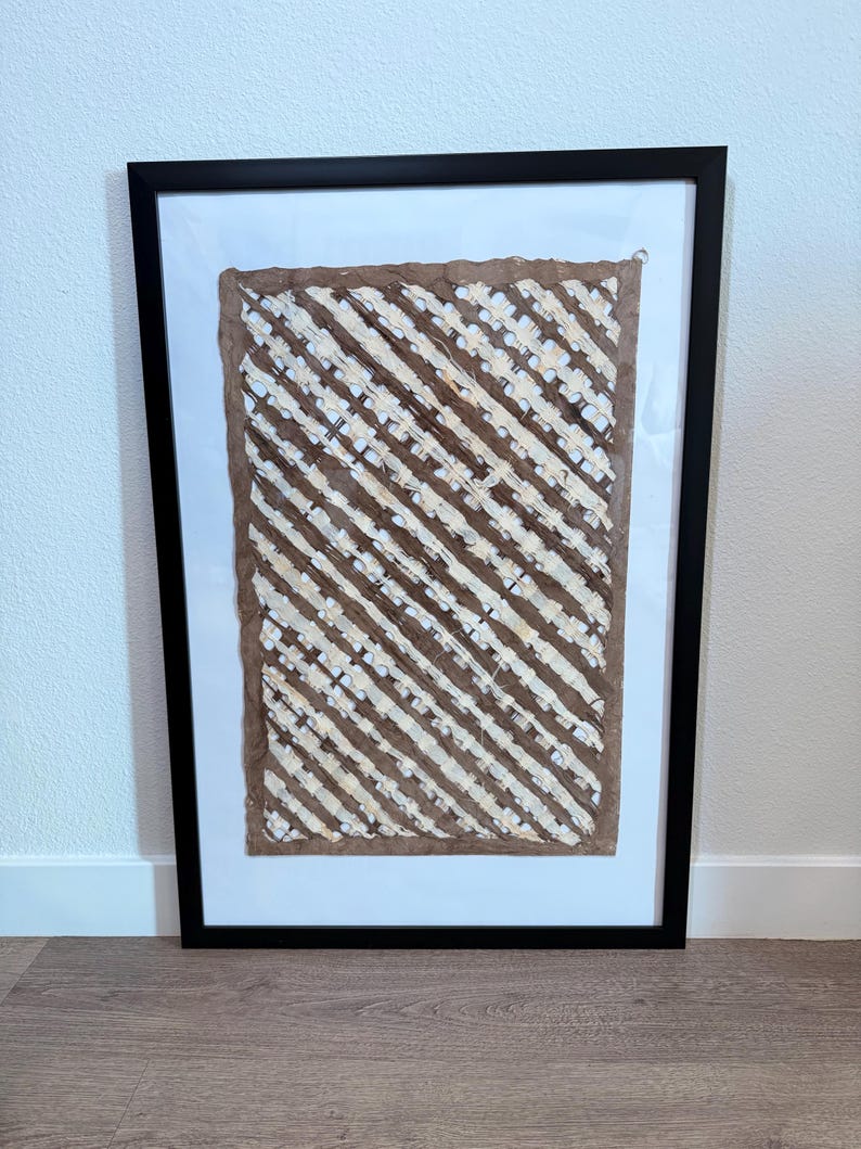 May include: Framed artwork featuring a textured, brown and white diagonal striped design. The artwork is set against a white background within a black frame. The piece is displayed on a wooden floor.
