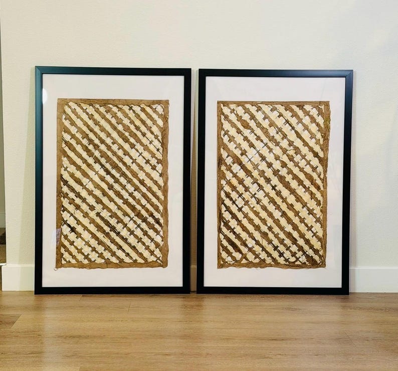 May include: Two framed artworks. Each piece features a textured, woven design in shades of beige and brown, set against a white background. The artwork is encased in a black frame, creating a striking contrast. The overall aesthetic is natural and earthy.