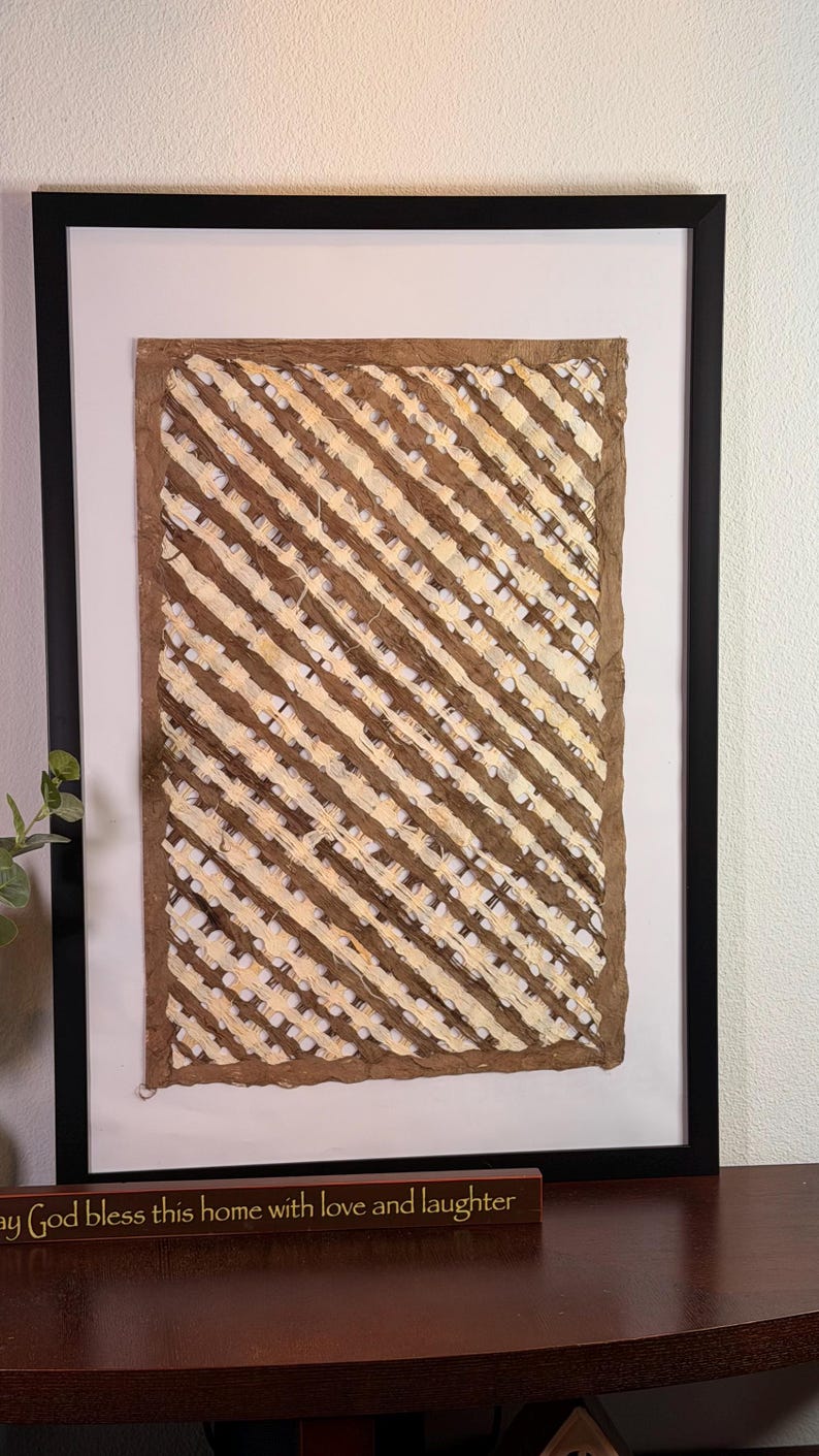 May include: Abstract artwork in a black frame. The art piece features diagonal stripes in shades of brown and cream. The artwork is displayed on a white background. A wooden sign below the artwork reads "May God bless this home with love and laughter."