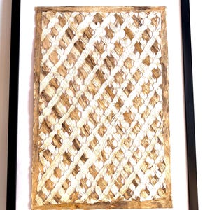 May include: Framed artwork featuring a woven, lattice-like design in natural beige and white tones. The artwork is encased in a white mat and a black frame, creating a modern and textured aesthetic. The piece is suitable for home decor.