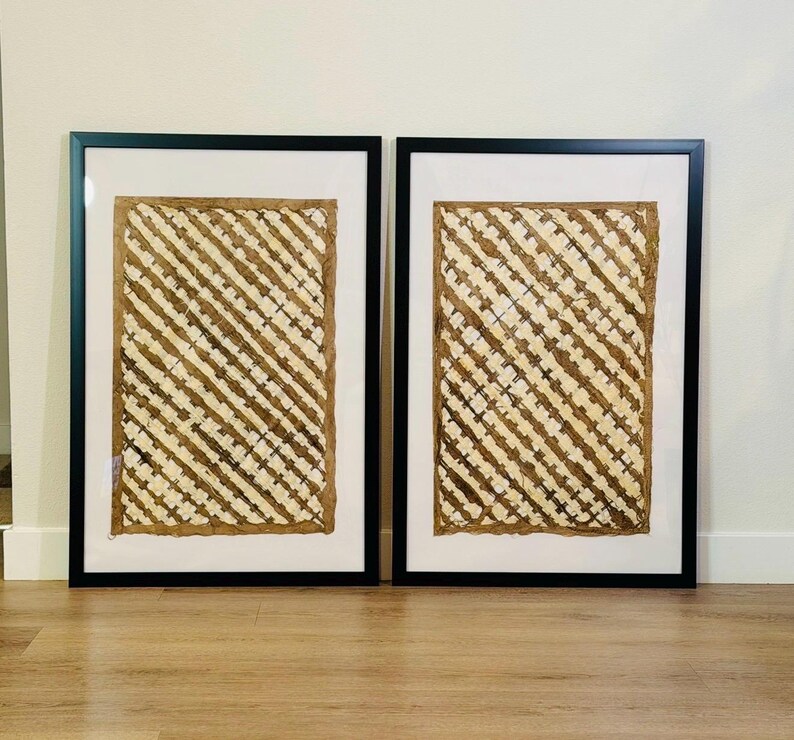 May include: Two framed artworks. Each piece features a textured, woven design in shades of beige and brown, set against a white background. The artwork is encased in a black frame, creating a striking contrast. The overall aesthetic is natural and earthy.