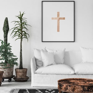 May include: A white couch with two pillows sits in front of a white wall with a framed print of a brown cross. A black and white patterned rug is on the floor in front of the couch. A round, copper-colored coffee table sits in front of the couch.