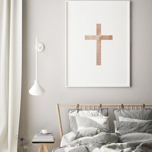 May include: A white framed print with a brown cross design on a white background. The print is hanging on a light gray wall above a bed with gray bedding and pillows.