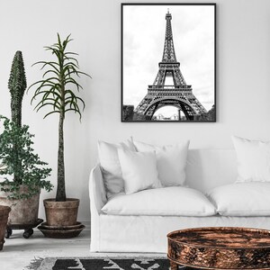 May include: A black and white photograph of the Eiffel Tower in Paris, France. The photo is framed in a black frame and is hanging on a white wall above a white couch.