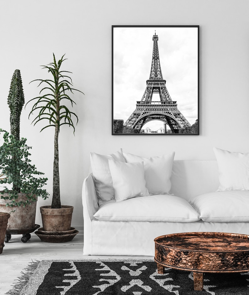 May include: A black and white photograph of the Eiffel Tower in Paris, France. The photo is framed in a black frame and is hanging on a white wall above a white couch.