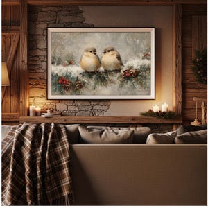 May include: A framed painting depicts two small birds perched on a snow-covered evergreen branch with red berries and pine cones. The artwork is displayed above a sofa with a plaid blanket, creating a cozy, rustic interior design.