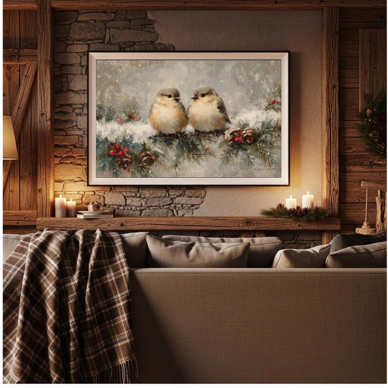 May include: A framed painting depicts two small birds perched on a snow-covered evergreen branch with red berries and pine cones. The artwork is displayed above a sofa with a plaid blanket, creating a cozy, rustic interior design.