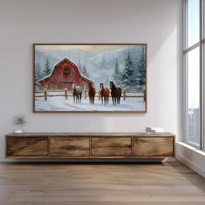 K&ouml;nnte beinhalten: Gerahmtes Gem&auml;lde einer verschneiten Winterlandschaft mit einer roten Scheune, die mit einem Kranz und Lichtern geschm&uuml;ckt ist. Vier Pferde stehen im Schnee vor der Scheune. Das Kunstwerk ist vor dem Hintergrund verschneiter B&auml;ume und Berge.