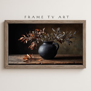 May include: A framed digital art print featuring a still life composition. A dark blue ceramic vase holds branches with brown and gray leaves. The vase sits on a wooden surface, with fallen leaves scattered nearby. The text "FRAME TV ART" is at the top.