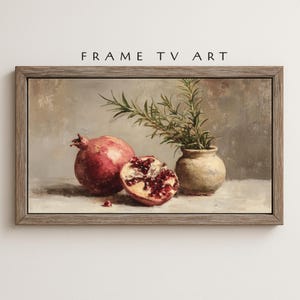 May include: A framed still life painting featuring a whole pomegranate and a halved pomegranate, displaying vibrant red seeds. A small, beige vase holds green sprigs. The text "FRAME TV ART" is at the top.