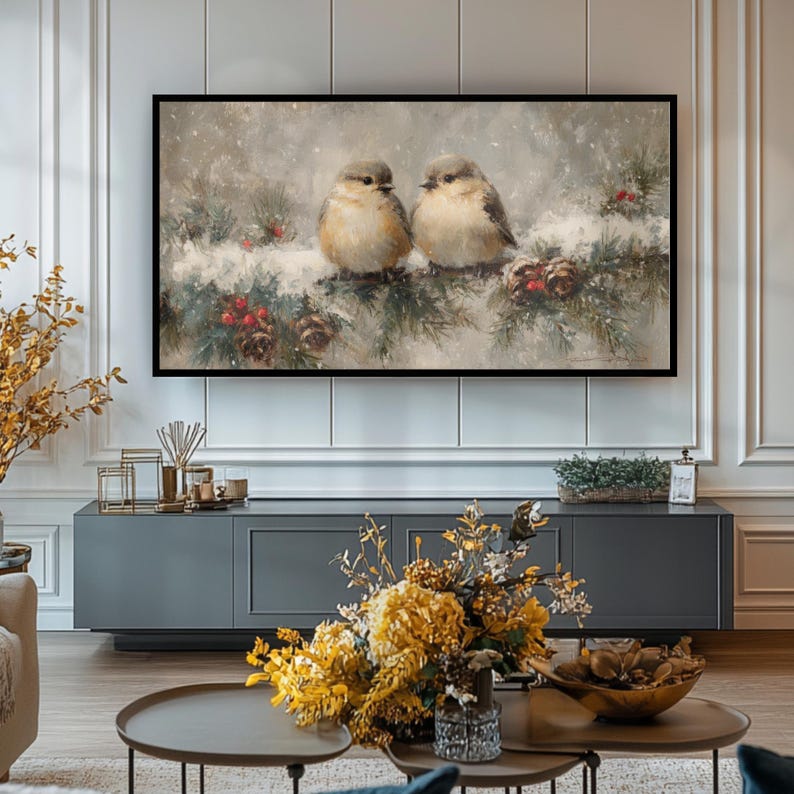 May include: A framed painting depicts two small birds perched on a snow-covered pine branch with red berries and pine cones. The artwork has a soft, muted color palette, creating a serene winter scene. The frame is black.