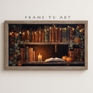 Puede incluir: Una obra de arte enmarcada que representa una escena de estantería acogedora. La imagen presenta una estantería de madera llena de libros antiguos, una vela encendida y pequeñas calabazas. El texto "FRAME TV ART" está en la parte superior.