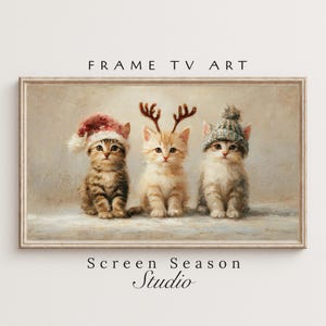 以下が含まれることがあります： 3匹の子猫が描かれた、額入りのデジタルアートプリント。サンタ帽をかぶった子猫、トナカイの角をつけた子猫、ニット帽をかぶった子猫がいます。「FRAME TV ART」と「Screen Season Studio」の文字が表示されています。