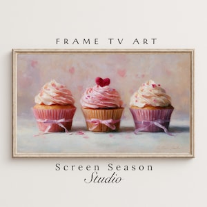 Könnte beinhalten: Gerahmtes Gemälde mit drei Cupcakes mit rosa Zuckerguss und dekorativen Schleifen. Ein Cupcake ist mit einem roten Herzen gekrönt. Der Hintergrund ist ein zartes Rosa mit Herzformen. Der Text "FRAME TV ART" und "Screen Season Studio" sind sichtbar.