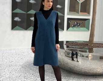 Peut inclure: Une robe bleue sans manches à col en V portée sur un haut noir à manches longues et col montant, associée à des collants noirs et des escarpins noirs à bout pointu. La robe présente une coupe droite arrivant aux genoux.