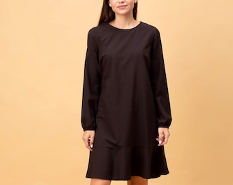 May include: A long-sleeved, dark brown dress with a round neckline and a ruffled hem. The dress is paired with black ankle boots. The model is standing in front of a light brown background.