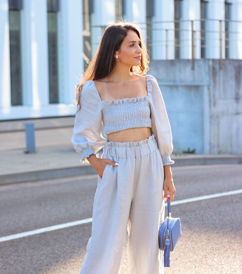 K&ouml;nnte beinhalten: Hellblaues Leinen-Ensemble, bestehend aus einem Crop-Top mit quadratischem Ausschnitt und langen, gerafften &Auml;rmeln. Passende hochtaillierte, weite Hose. Eine kleine, quadratische, hellblaue Handtasche mit Quaste.