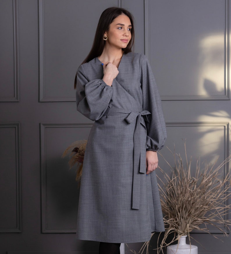 May include: A gray wrap dress with long, voluminous sleeves and a matching tie belt. The dress has a V-neckline and a knee-length hem. The fabric appears to be a woven material. The dress is a solid color and suitable for various occasions.