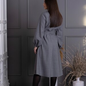 May include: A gray dress with long sleeves and a belted waist. The dress has a knee-length skirt and is paired with black tights and high-heeled shoes. The dress is made of a textured fabric and is suitable for formal occasions.