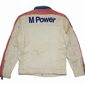 May include: A white jacket with red and blue accents. The jacket has a zip fastening and an "M Power" logo on the back.