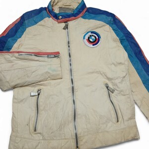 May include: A white leather jacket with blue, pink and light blue stripes on the sleeves. The jacket has a zip fastening and a BMW logo patch on the chest.