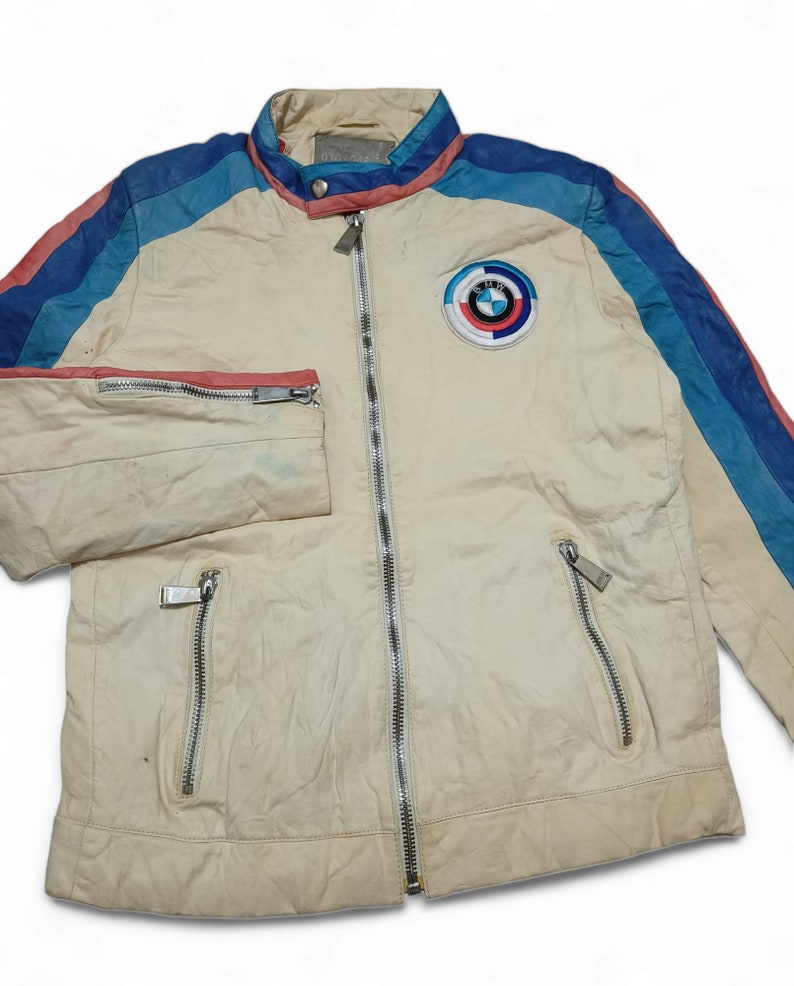 May include: A white leather jacket with blue, pink and light blue stripes on the sleeves. The jacket has a zip fastening and a BMW logo patch on the chest.