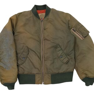 Puede incluir: Chaqueta bomber verde oliva con cremallera completa, dos bolsillos delanteros y un bolsillo con cremallera en la manga izquierda. La chaqueta tiene pu&ntilde;os de canal&eacute; verde oscuro y un cuello a juego. El interior es naranja.