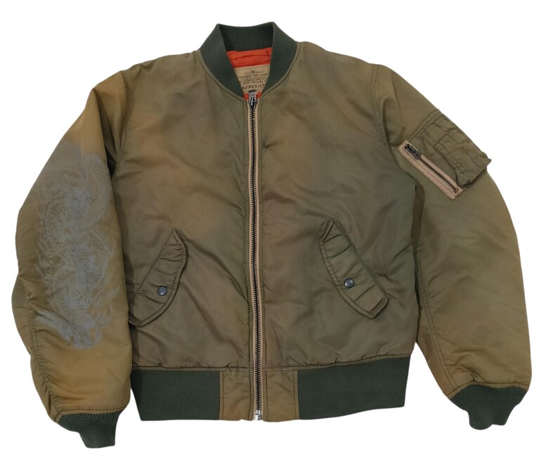 Puede incluir: Chaqueta bomber verde oliva con cremallera completa, dos bolsillos delanteros y un bolsillo con cremallera en la manga izquierda. La chaqueta tiene pu&ntilde;os de canal&eacute; verde oscuro y un cuello a juego. El interior es naranja.