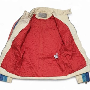 May include: A white leather jacket with a red quilted lining. The jacket has a zip fastening and a collar. The sleeves have a blue, white and red striped pattern.