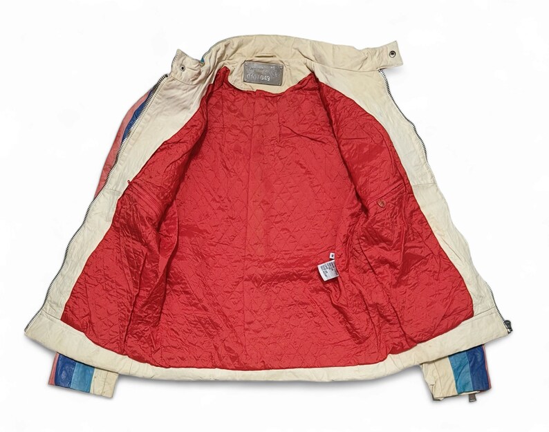 May include: A white leather jacket with a red quilted lining. The jacket has a zip fastening and a collar. The sleeves have a blue, white and red striped pattern.