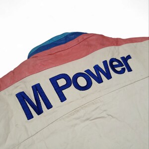 May include: A white jacket with a blue, pink and teal striped collar. The back of the jacket has "M Power" embroidered in blue.