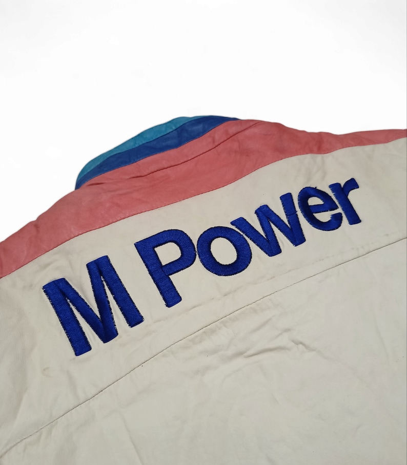May include: A white jacket with a blue, pink and teal striped collar. The back of the jacket has "M Power" embroidered in blue.