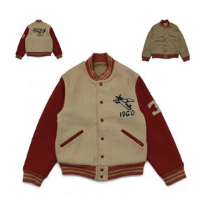 Könnte beinhalten: Eine cremefarbene und rote Collegejacke mit einem dunkelblauen Flugzeug und "1960" bestickt auf der Vorderseite. Die Ärmel sind rot mit einem weißen Streifen und die Nummer "3" ist auf dem rechten Ärmel gestickt.