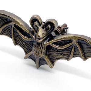 May include: A bronze-coloured bat-shaped cabinet knob. The bat has detailed wings and a textured body. The knob is designed to be attached to a cabinet or drawer. The hardware has a vintage or antique appearance.