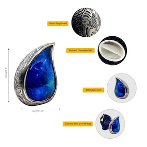 Op de afbeelding: Een blauwe en zilveren traanvormige crematie urn met een handgegraveerd ontwerp. De urn heeft een schroefdeksel en wordt geleverd met een fluwelen zak. Hij is 15,2 cm hoog en 11,4 cm breed.