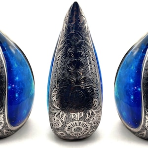 Op de afbeelding: Drie traanvormige urnen met een blauw en zwart galaxy-ontwerp. De urnen zijn gemaakt van keramiek en hebben een ingewikkeld bloemmotief.