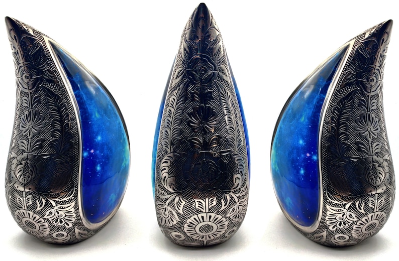 Op de afbeelding: Drie traanvormige urnen met een blauw en zwart galaxy-ontwerp. De urnen zijn gemaakt van keramiek en hebben een ingewikkeld bloemmotief.