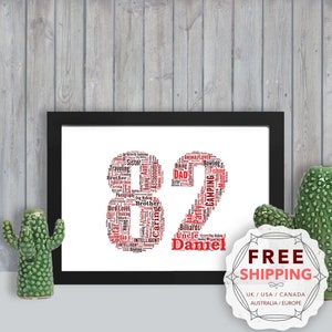 May include: A framed print with a red and black word cloud in the shape of the number 82. The word cloud includes words like "brother", "camping", "fishing", "dad", and "uncle". The name "Daniel" is written below the number. The print is on a white background and is framed in black.