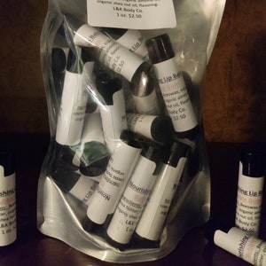 May include: A clear plastic bag containing numerous small tubes of lip balm. The tubes are labelled 'Nourishing Lip Balm Bubble Gum' and list the ingredients: Beeswax, organic cocoa butter, organic almond oil, organic shea nut oil, flavouring. The label also states 'L&K Body Co. 1 oz. £2.50'