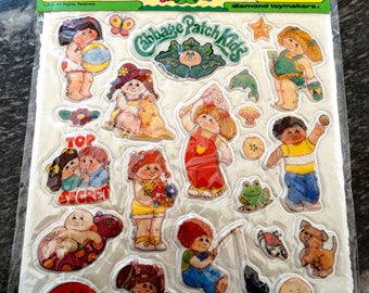 Puede incluir: Una hoja de pegatinas hinchadas con personajes de Cabbage Patch Kids. Las pegatinas son coloridas y presentan varios personajes en diferentes poses. Las pegatinas están diseñadas para ser usadas en un libro de bebé Cabbage Patch Kids.