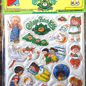 Op de afbeelding: Een pakketje puffy Cabbage Patch Kids stickers. De stickers tonen verschillende Cabbage Patch Kids karakters en zinnen zoals "Snack Time" en "Cutie Pie". De verpakking bevat de tekst "Puffy Stick-Ons".