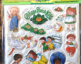 Pode incluir: Um pacote de adesivos fofos Cabbage Patch Kids. Os adesivos apresentam vários personagens e frases Cabbage Patch Kids como "Snack Time" e "Cutie Pie". A embalagem inclui o texto "Puffy Stick-Ons".