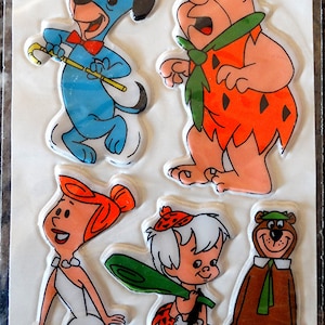 Puede incluir: Un conjunto de siete pegatinas hinchadas con personajes de dibujos animados de Hanna-Barbera. Las pegatinas incluyen a Fred Flintstone, Wilma Flintstone, Pebbles Flintstone, Dino, Huckleberry Hound y un dinosaurio morado. Las pegatinas están sobre un fondo blanco con un borde de arcoíris.