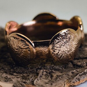 Könnte beinhalten: Ein Kupferring mit einem strukturierten, kreisförmigen Design. Der Ring besteht aus mehreren verbundenen Kreisen, die jeweils eine erhabene, strukturierte Oberfläche haben.