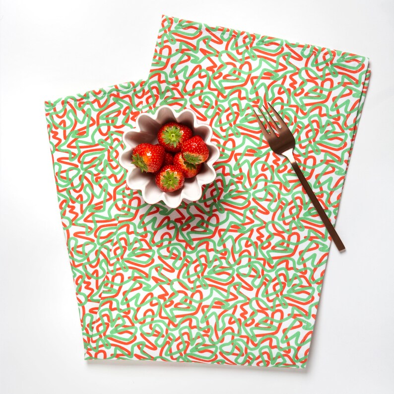 May include: A white bowl with red strawberries on a white and green patterned fabric with a gold fork.