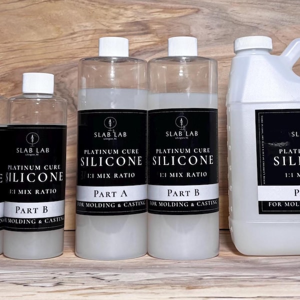 May include: Eight clear plastic bottles of Slab Lab Platinum Cure Silicone for molding and casting, arranged in four pairs of increasing size. Each bottle features a black label with white text indicating Part A or Part B and a 1:1 mix ratio.